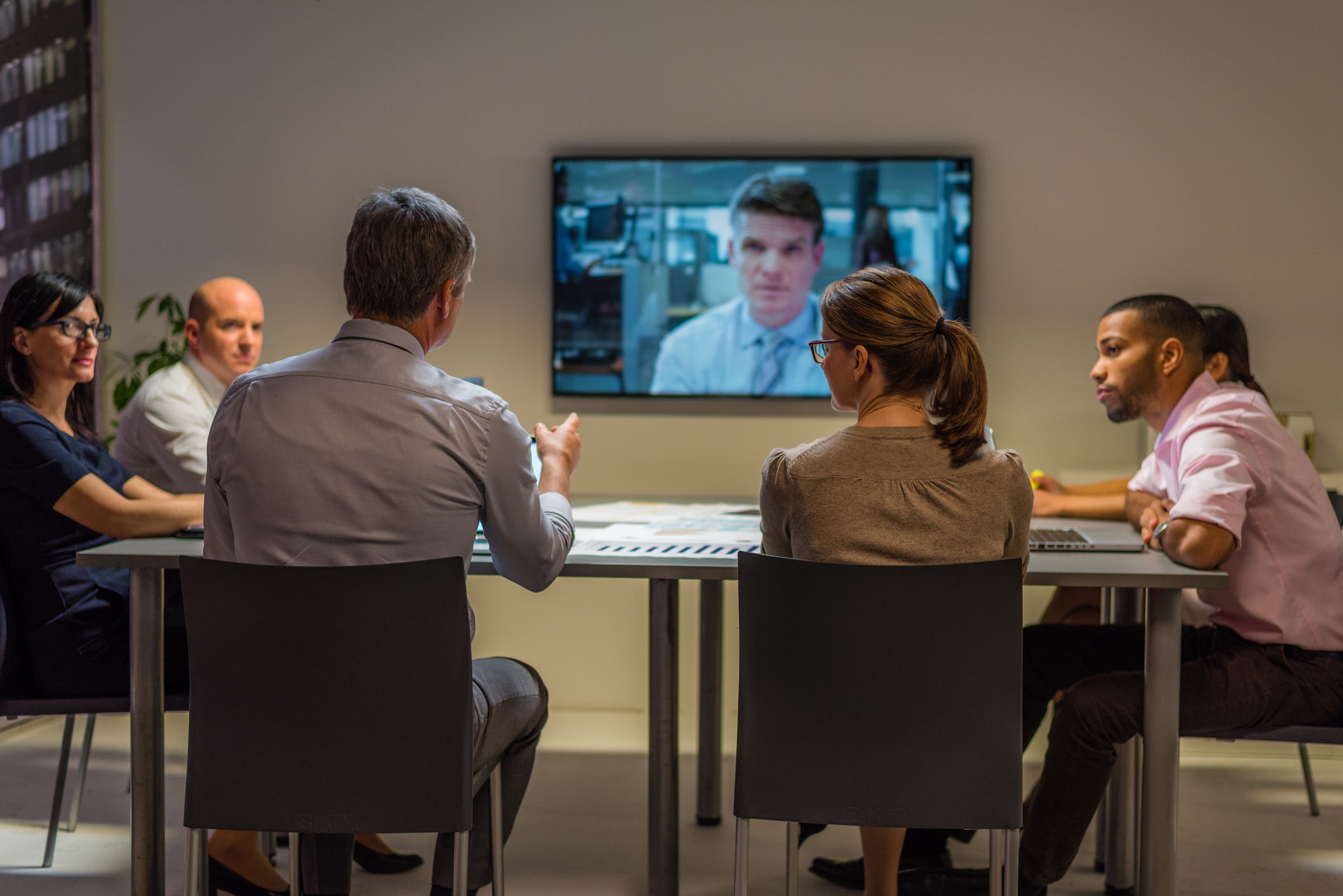 Business people sitting and discussing in board room during video conference meeting.