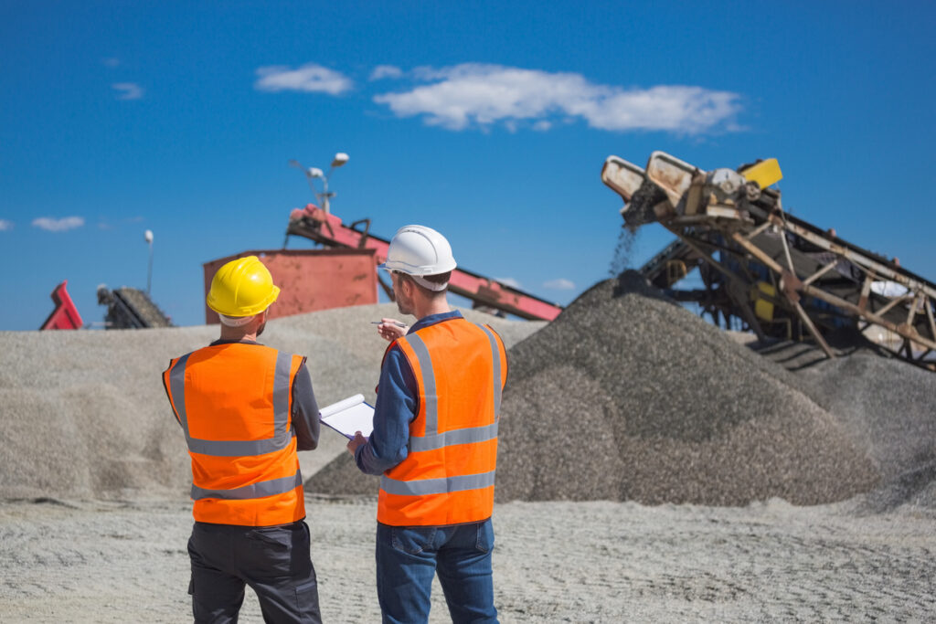 Two workers, in safety apparel, observe operations at an open-pit mine