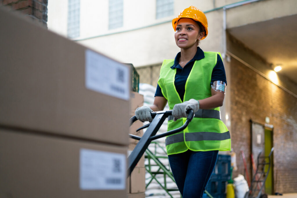 Female employee using a pallet jack to move boxes in a warehouse