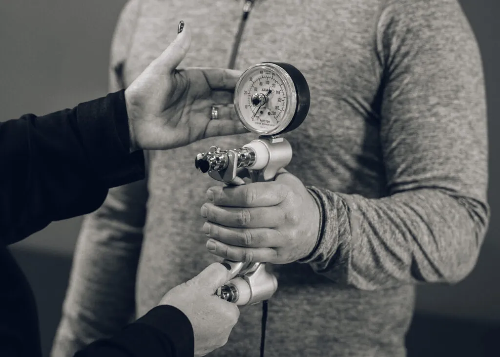 Employee is using calipers to test for grip strength while being monitored by a therapist.