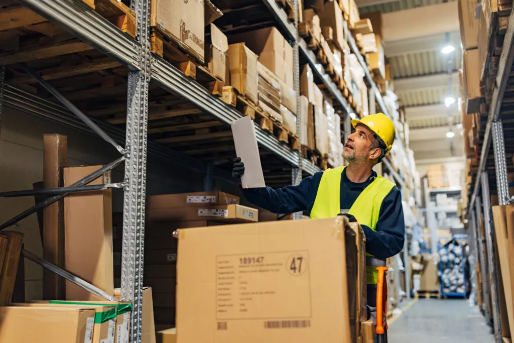 Mature worker with clipboard checking delivery, stock in warehouse.