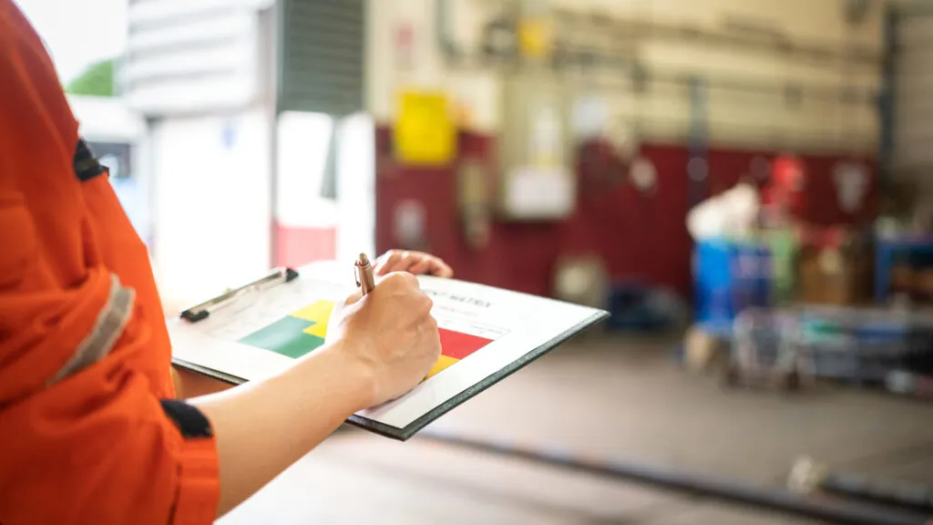 A manager is holding a pen and risk matrix form with factory workshop place as blurred background.