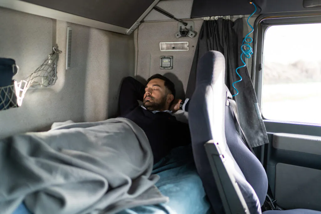 Truck driver sleeping in cabin bed on truck stop
