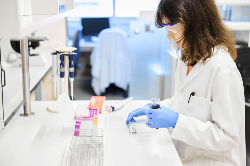 Focused young female scientist in goggles and uniform analysing a sample while conducting research in the laboratory.